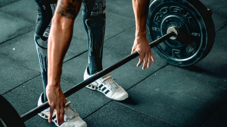 Deportista levantando barra en gimnasio, artículo sobre acupuntura para lesiones deportivas en QiSport